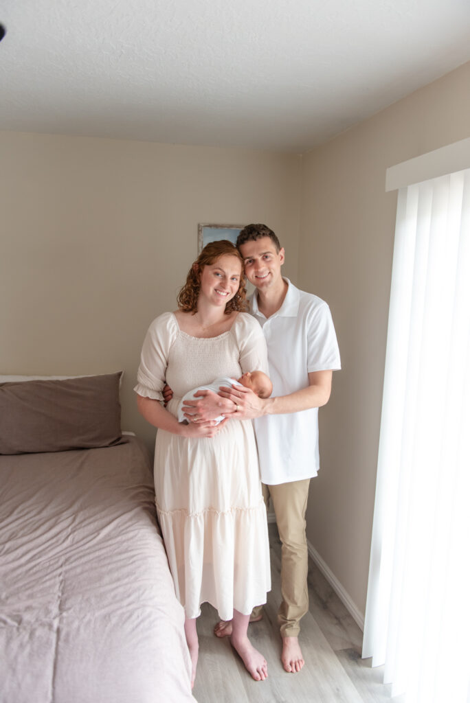 Mother holding newborn near window with soft natural light during lifestyle photo session at home in St. George