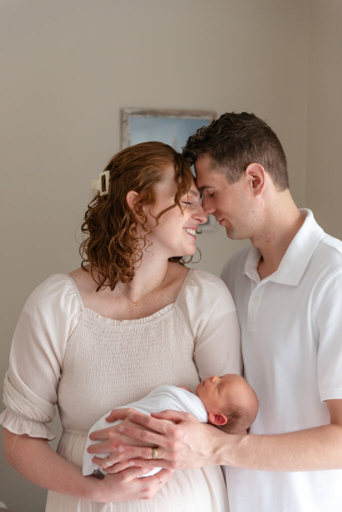 Mother and father touching foreheads while holding newborn baby during emotional in-home session in St. George