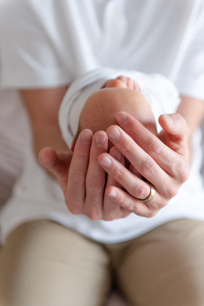 Close-up of father’s hands gently cradling newborn’s head during lifestyle newborn session in Southern Utah