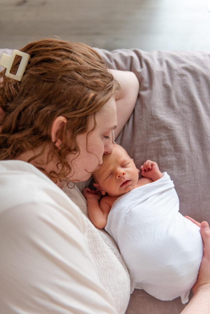 Mother kissing newborn on bed during intimate in-home newborn photo session in St. George, Utah