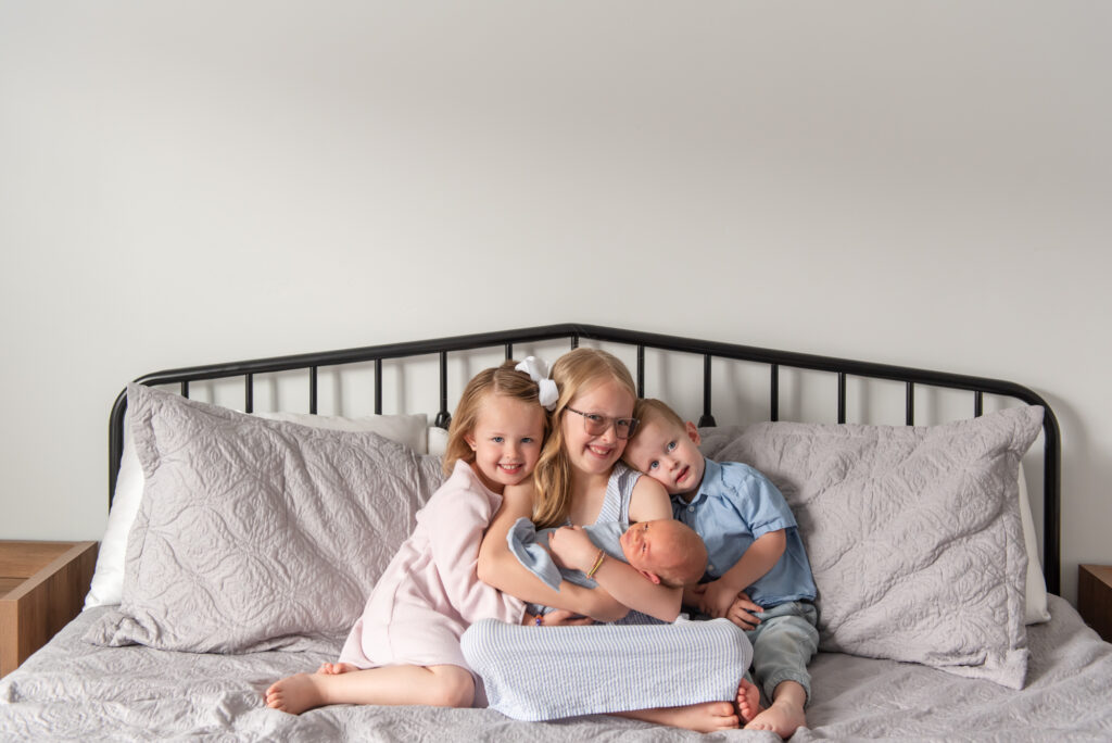 Big sisters and brother cuddling newborn baby brother during lifestyle newborn photography session