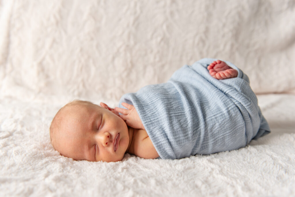 Newborn baby wrapped in swaddle with tiny feet showing during minimalist photo session