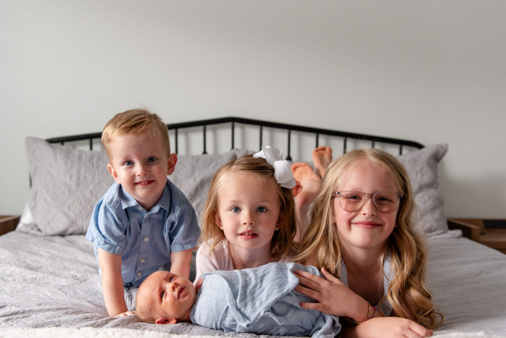 Children laying on bed with newborn baby brother during natural light newborn session