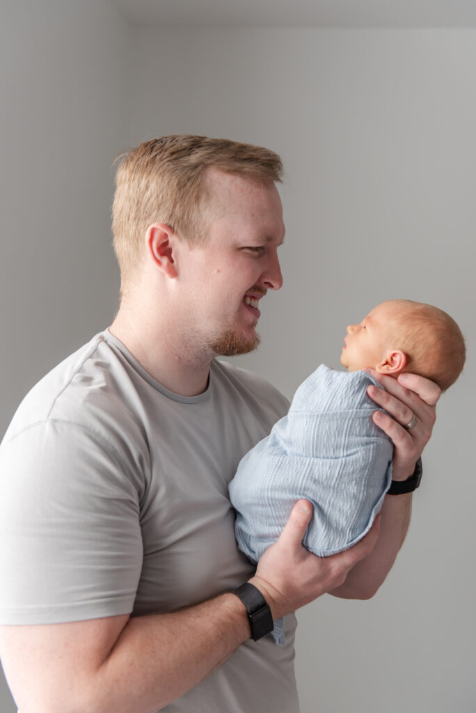 Father admiring newborn son during peaceful in-home newborn photography session