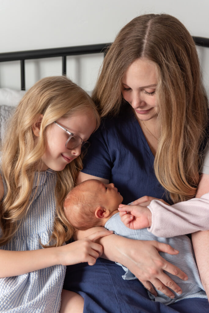 Mother and daughter bonding while holding newborn baby boy during in-home session