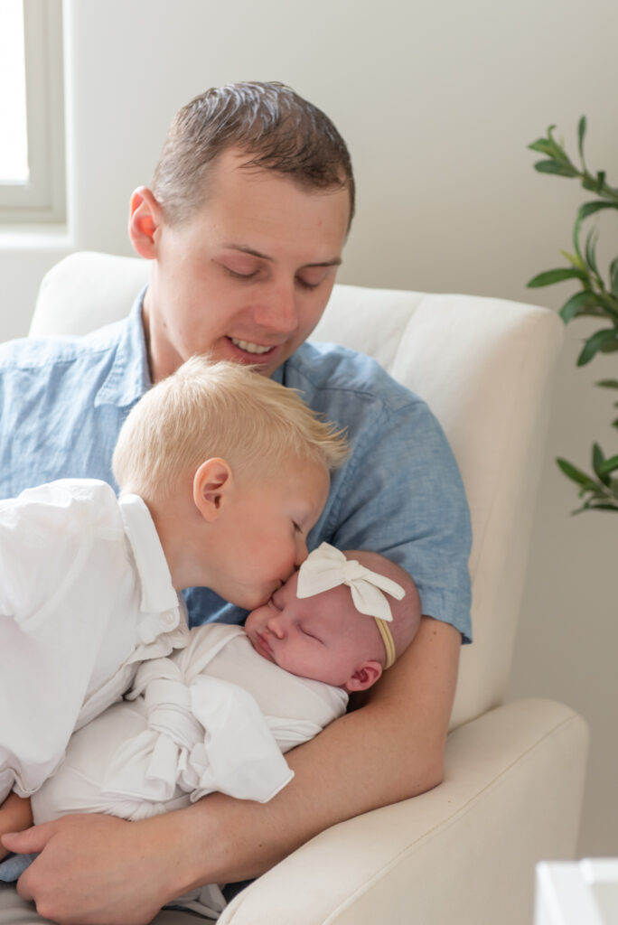 Big brother kissing newborn sister while Dad adores them in St. George, Utah