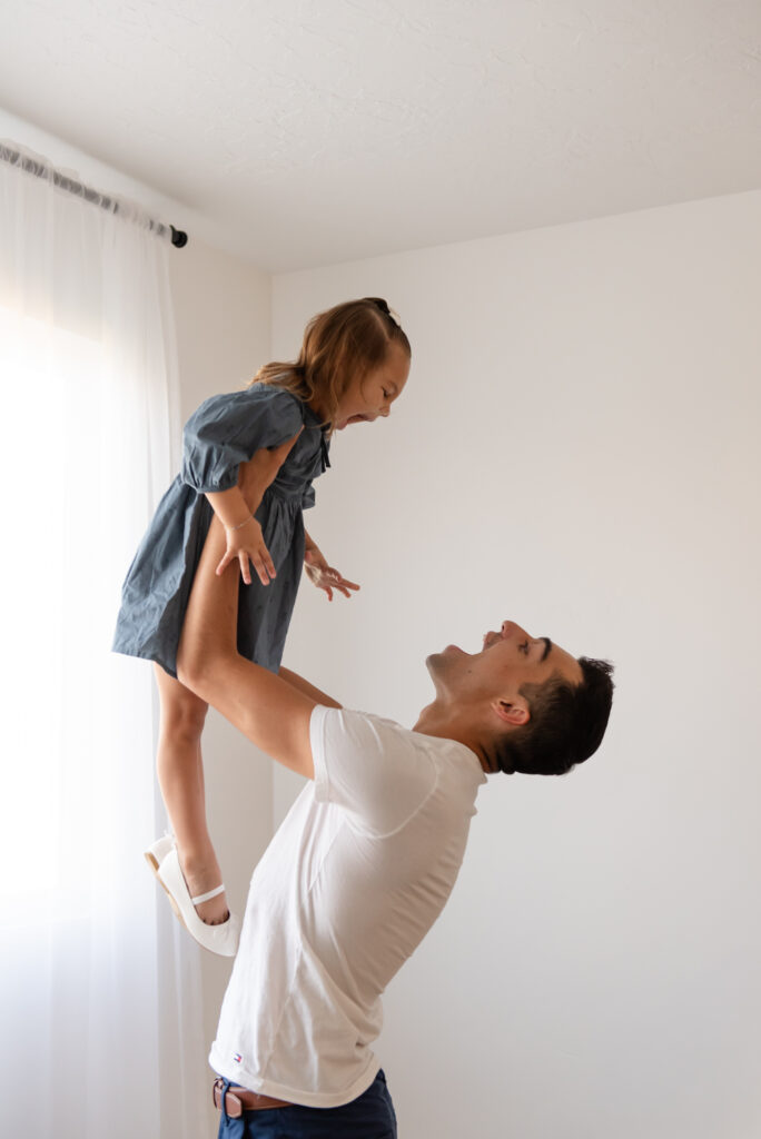 Family maternity photos in Southern Utah – dad tossing toddler girl in the air with laughter