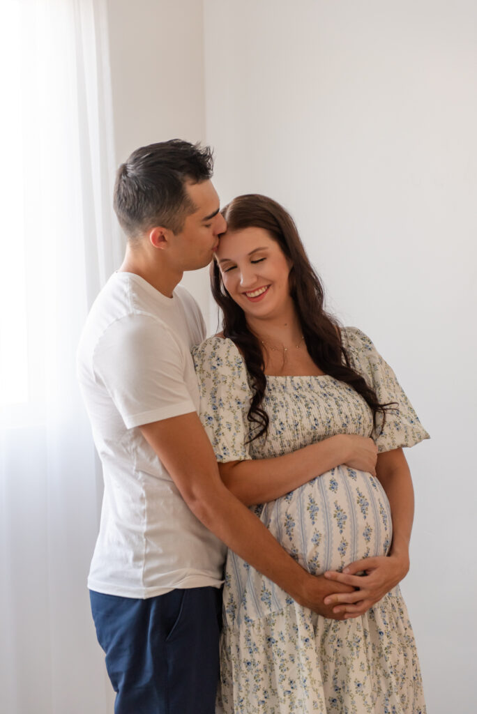 Maternity photography in Hurricane Utah – mom in glowing dress holding baby bump with dad at The Studio Hurricane