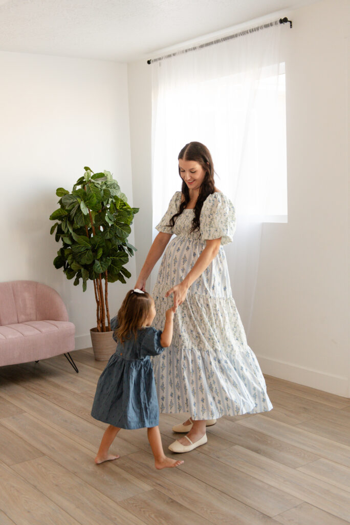 Studio maternity session in Hurricane Utah – mom twirling daughter in natural window light