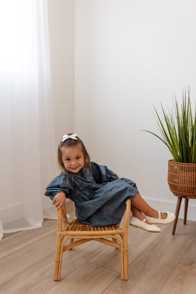 Toddler girl smiling on cute chair during maternity photos at The Studio Hurricane