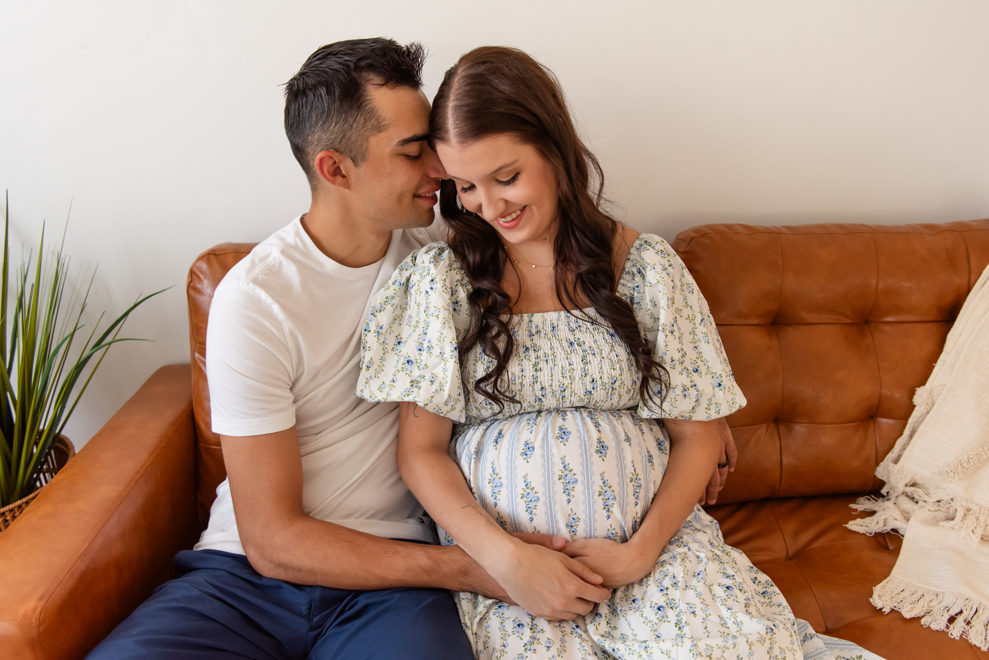 Mom and dad snuggled on brown leather couch for Southern Utah Maternity Photos